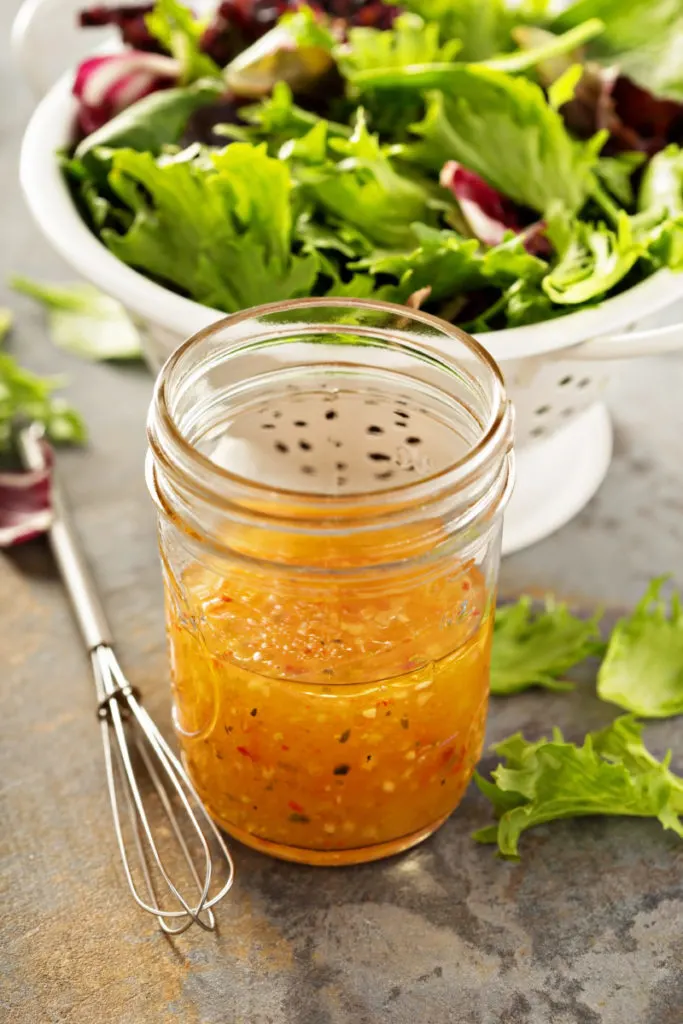 A mason jar with homemade salad dressing in it, a salad behind it.