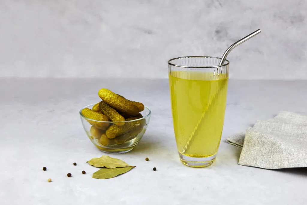 A small dish of pickles and a glass of pickle juice with a straw.