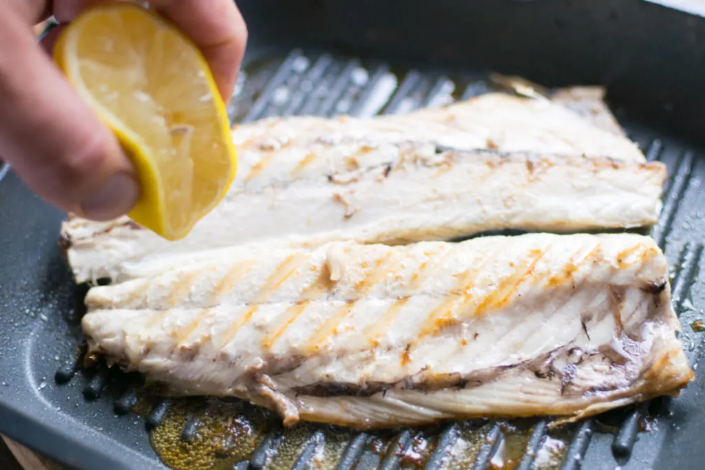  A hand is squeezing a lemon over grilled fish.