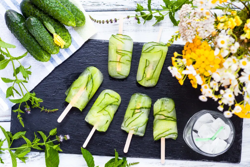 Pickle popsicles decoratively laid out on a piece of slate with herbs around. 