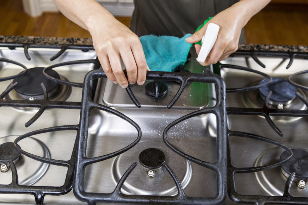 Hands shown holding a spray bottle and cleaning a gas range.