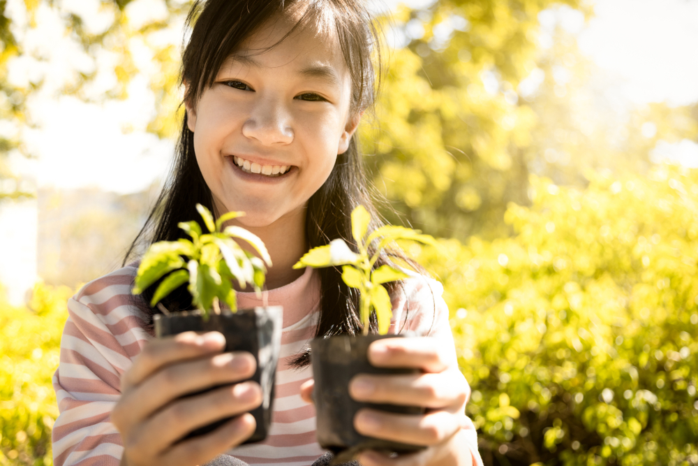 A young, smiling girl holds two seedlings up to the camera.