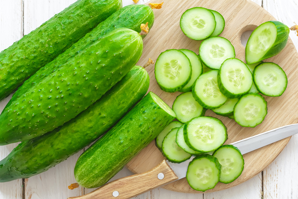 Several whole cucumbers sit next to cucumber slices on a cutting board.
