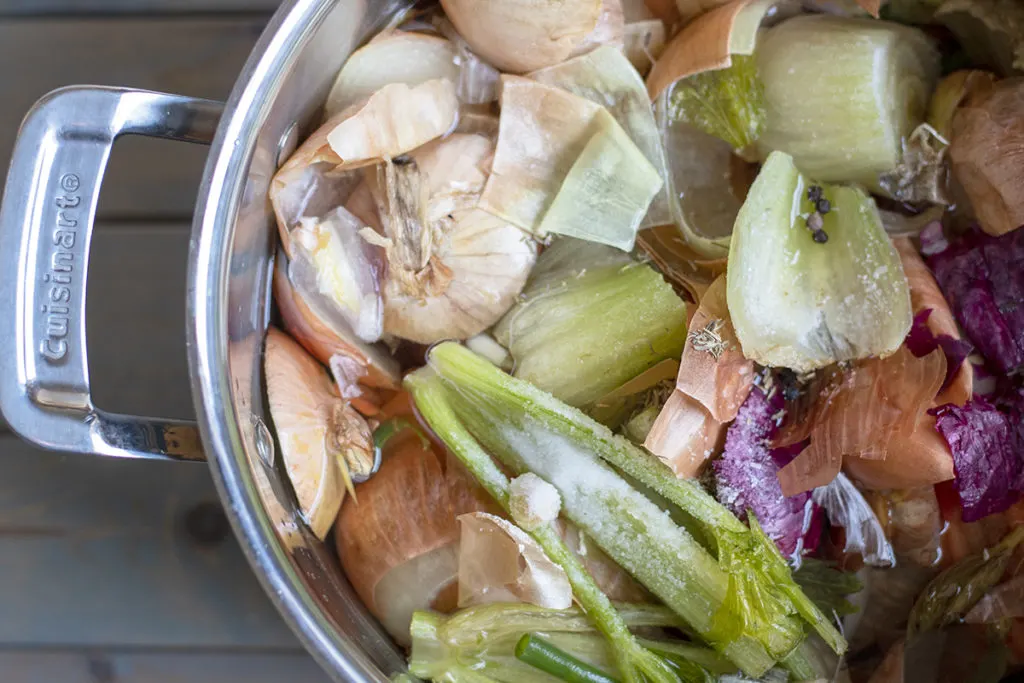 A close up of kitchen scraps in a stockpot with salt, spiced and water.