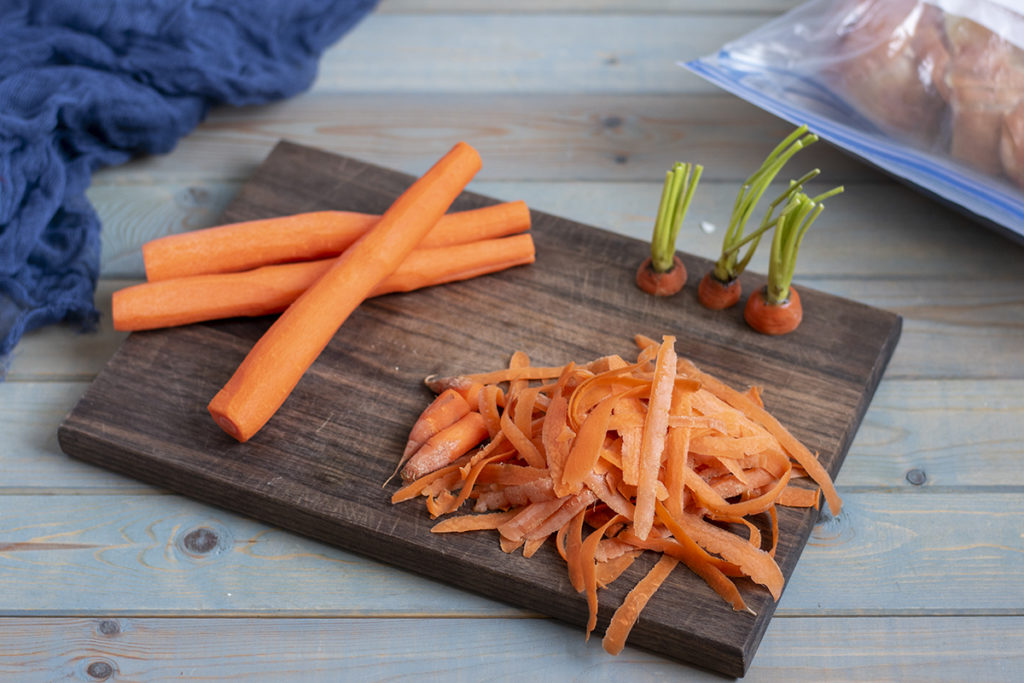 A cutting board with carrots and carrot peels and tops.