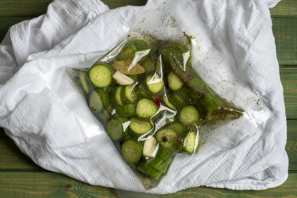A bag of refrigerator pickles vacuum sealed in a bag laying on a white tea towe.