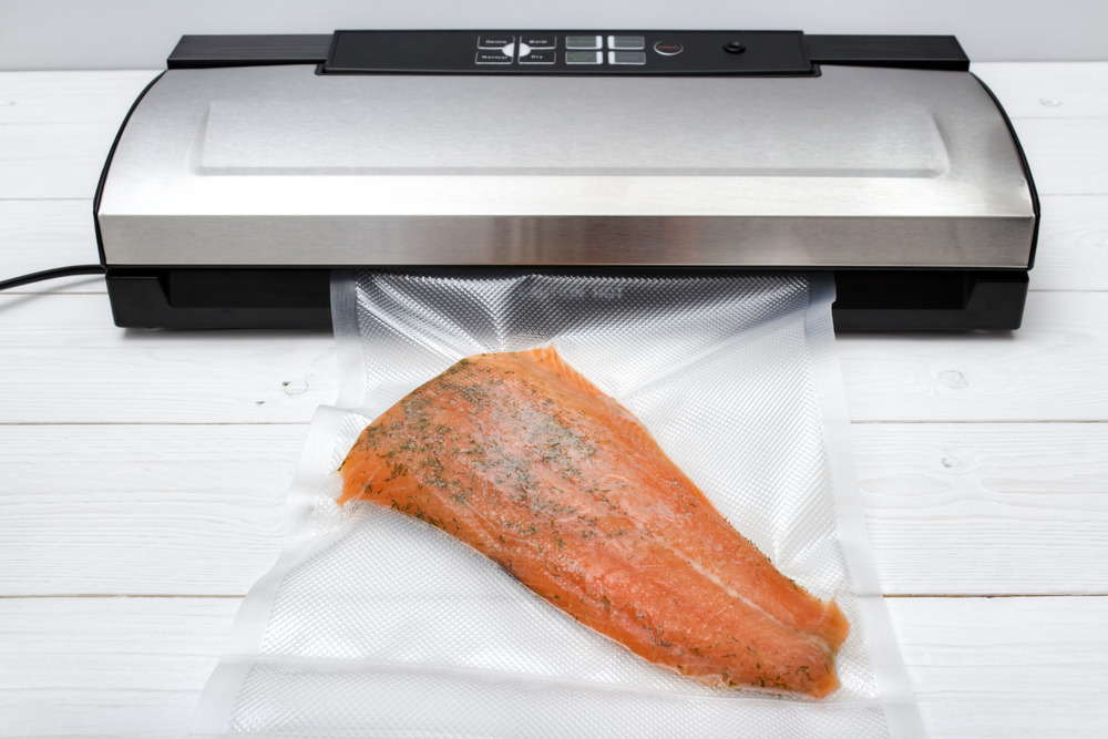 Vacuum sealer set up on a white wooden table. Salmon sealed in bag. 