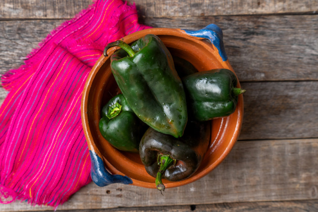 Four poblano peppers in a clay pot with a bright pink hand-woven towel. 