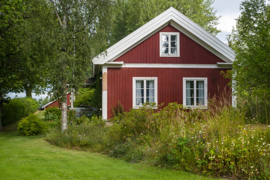 A red farmhouse with a portion of the lawn mowed and a portion of the lawn full of wildflowers and grasses.
