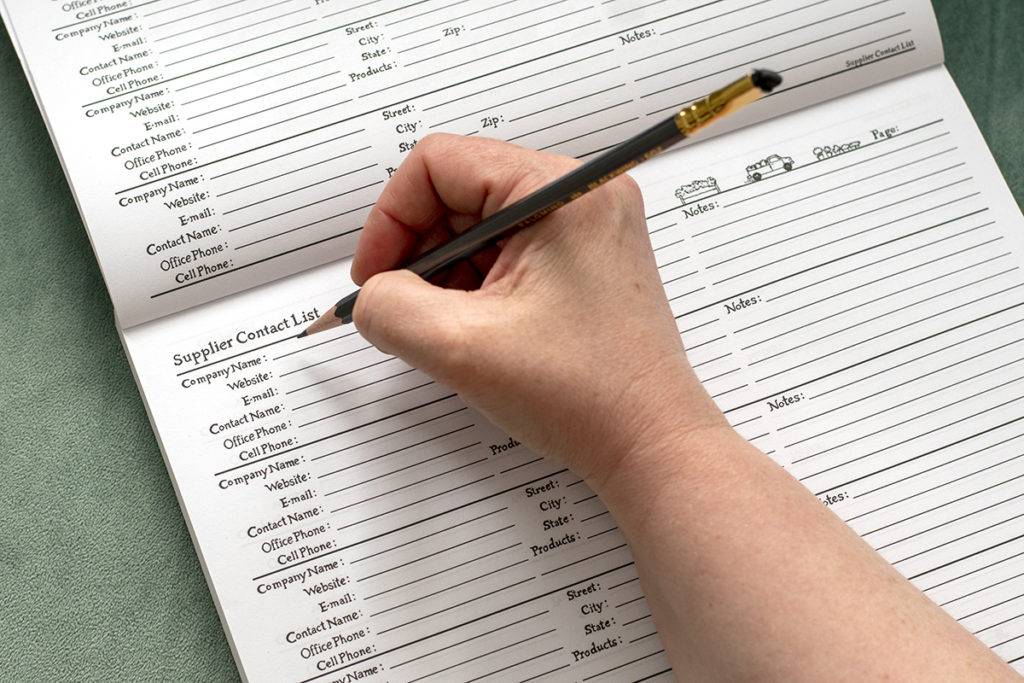 A handholding a pencil ready to fill in a Supplier Contact List page in a garden planner.