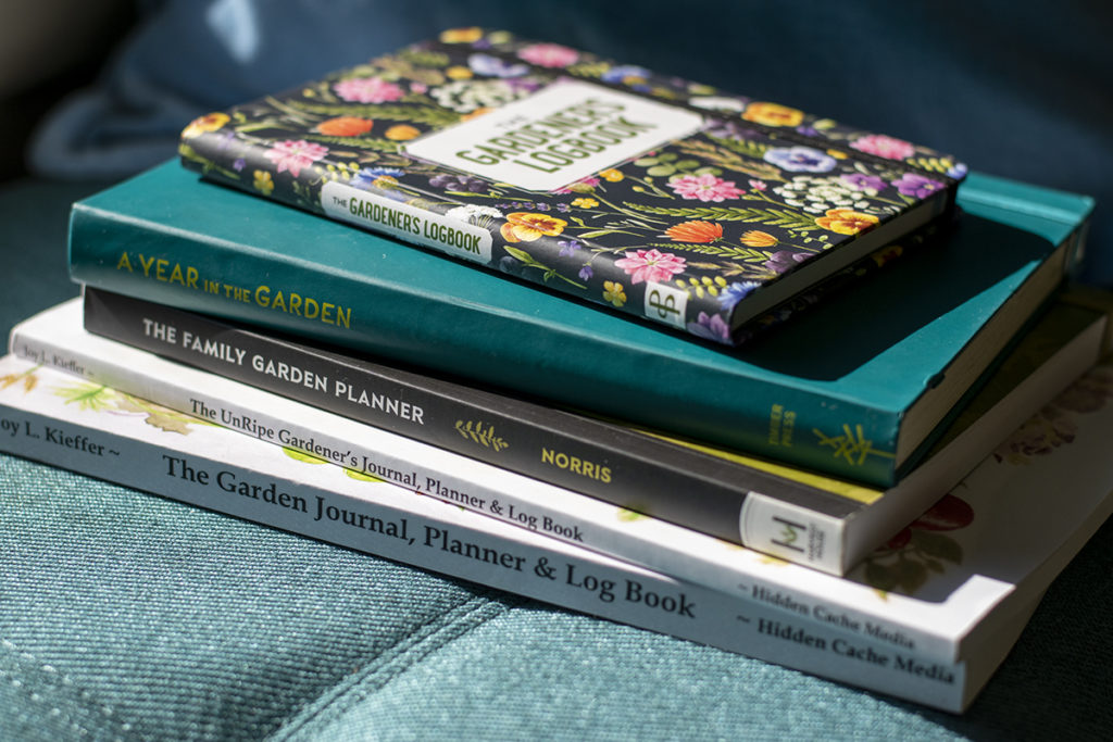 A stack of garden planners in the sunshine on a cushioned bench seat.