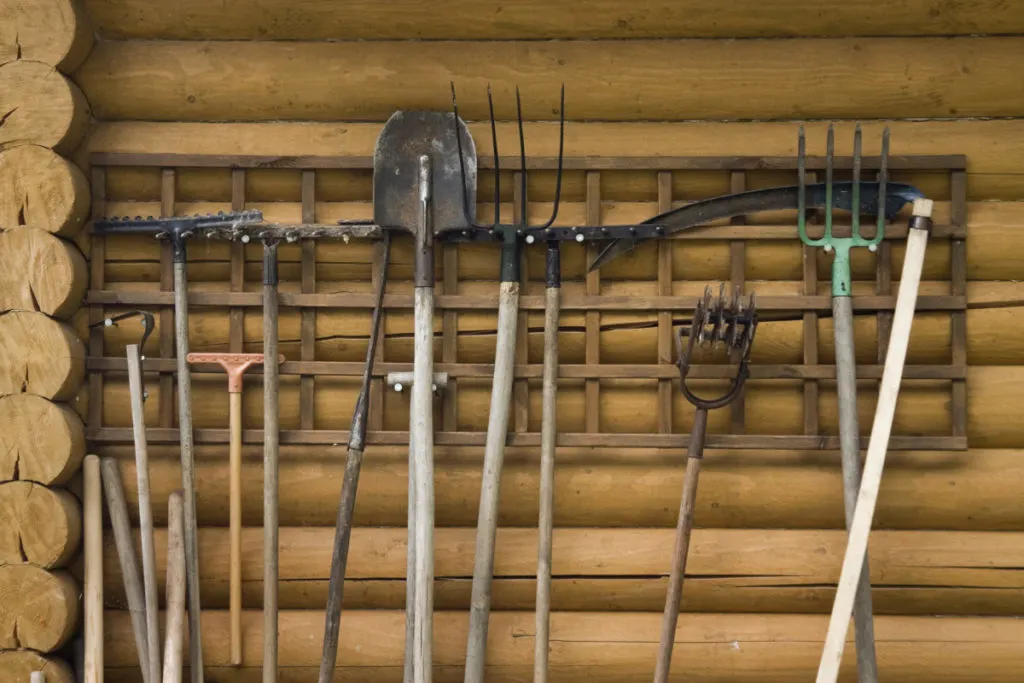 Garden tools lined up against a log cabin.