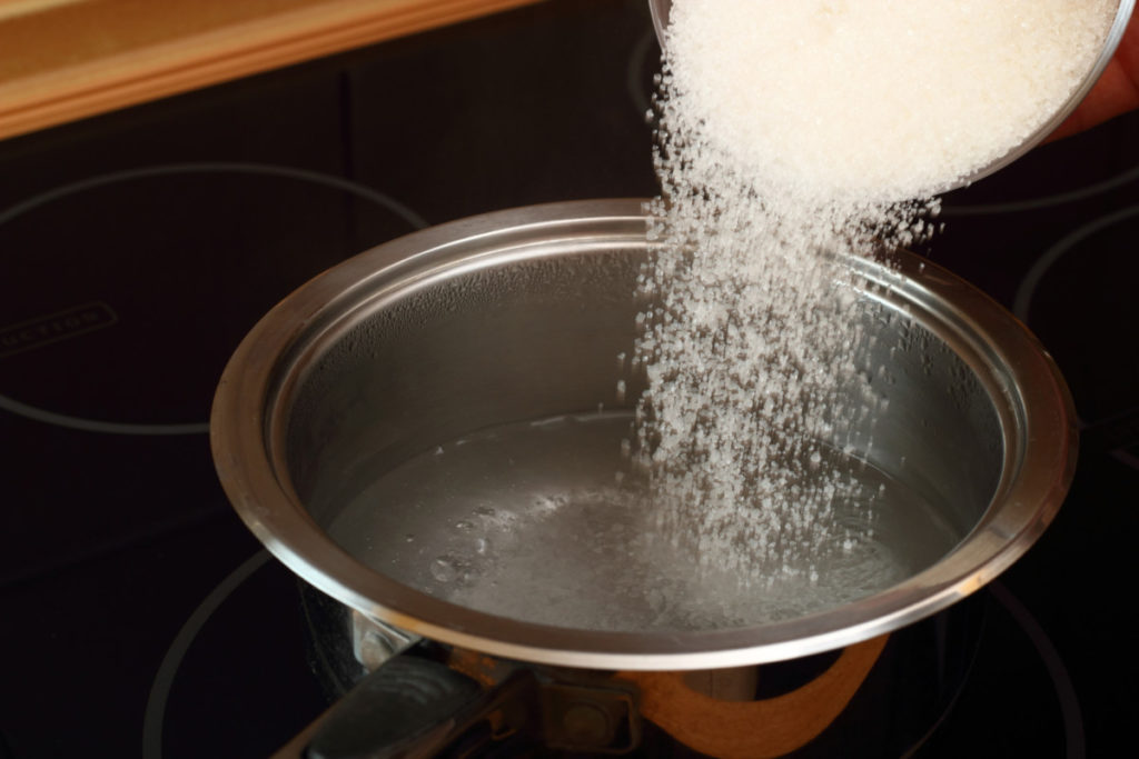 Sugar being poured into a pot of boiling water.