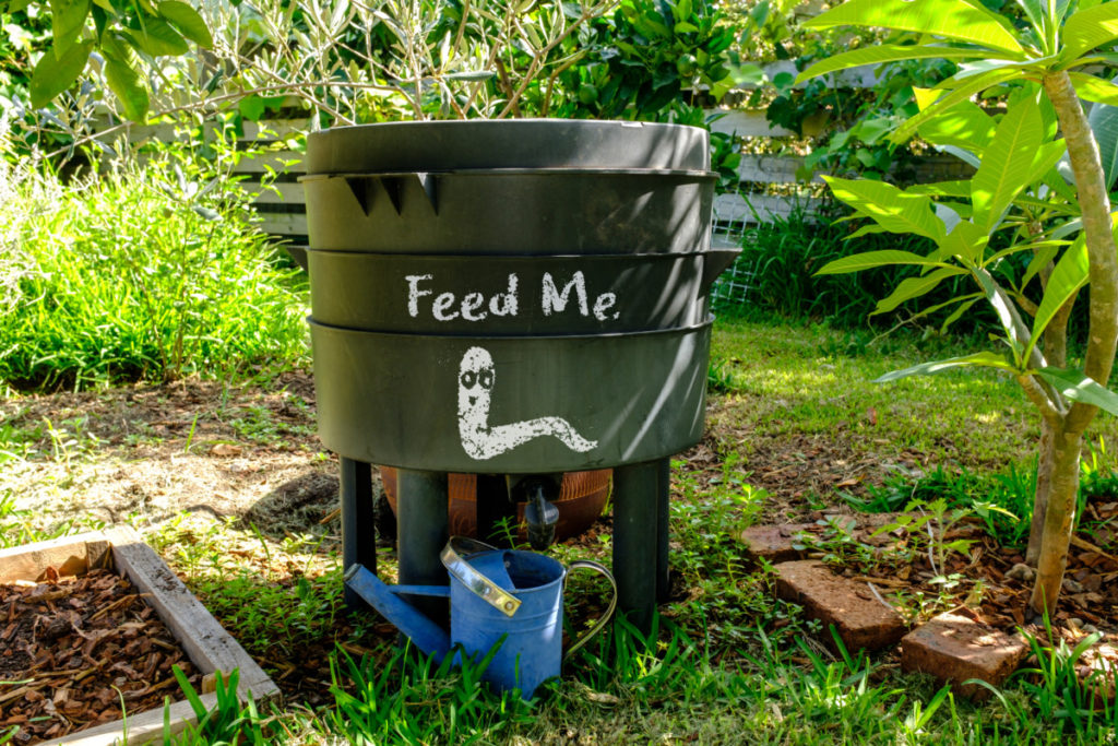 A compost bin with a worm and the words 'feed me' painted on the side.