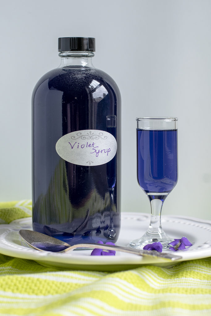 A bottle and a small cordial glass are filled with deep blue-purple violet syrup.