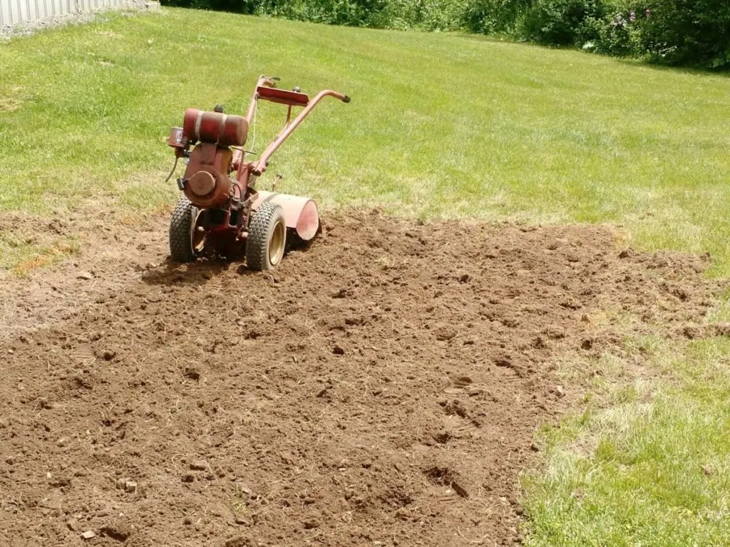 A red rototiller sits next to a stretch of newly tilled lawn.