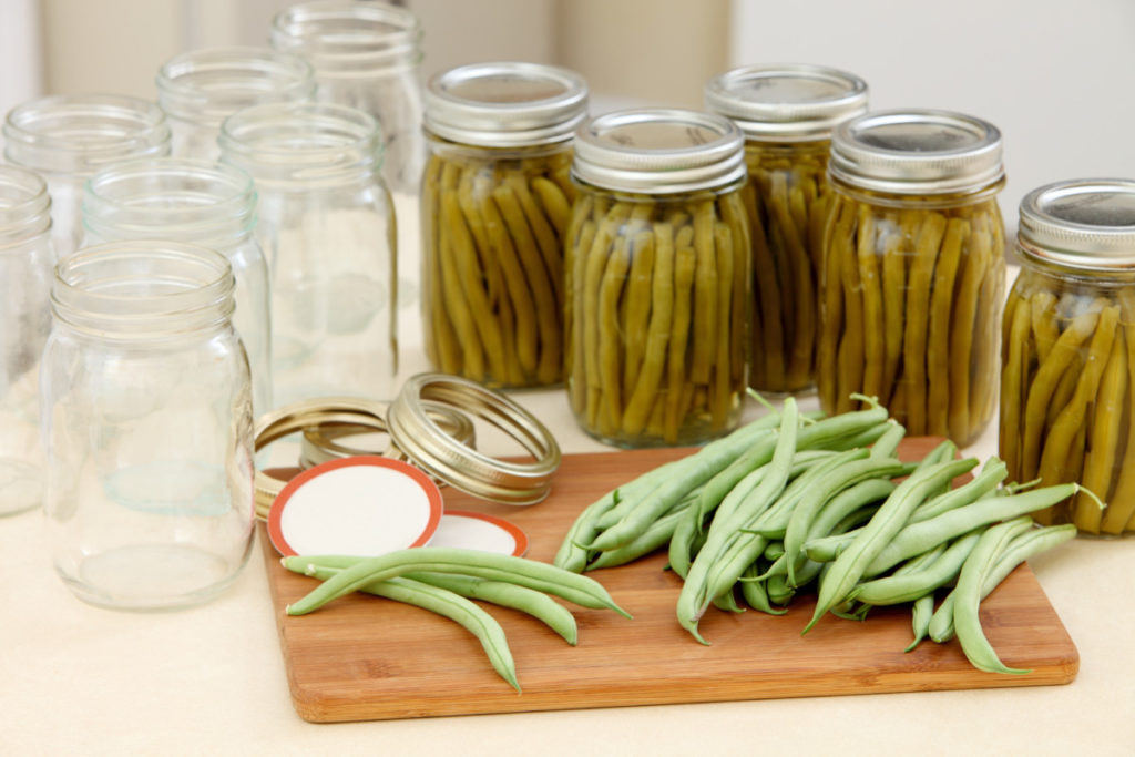 Canned green beans next to empty jars and raw green beans on a cutting board.