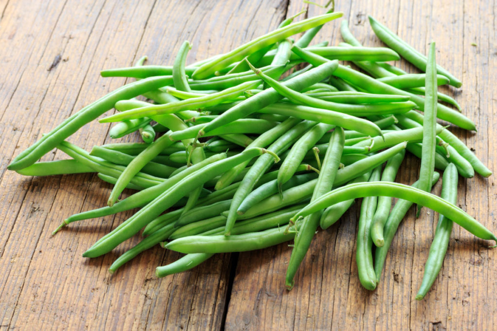 A pile of freshly picked green beans on a wood table.