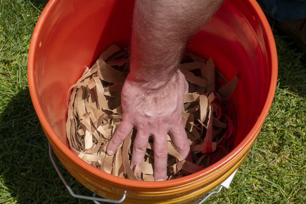 A man's hand is adding shredded paper bags to a bucket.