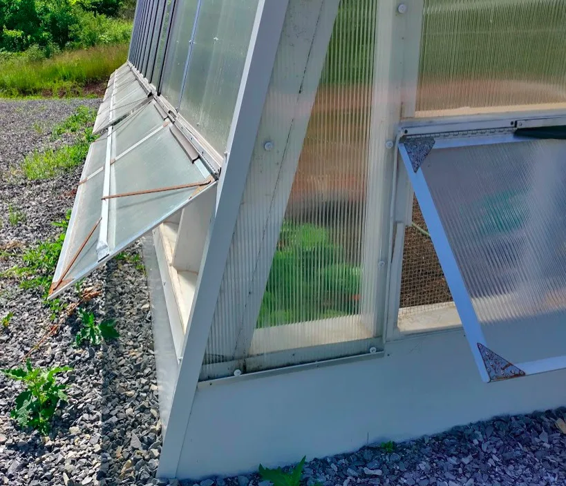 A close-up of the sustainable greenhouse's experimental vent system. The vents are open in the heat of the day. Some green plants are visible inside the greenhouse.