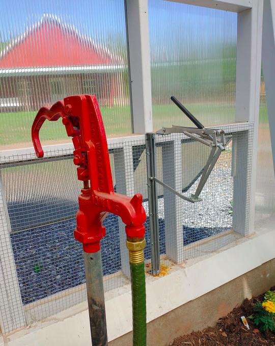 A bright red water hydrant with a green hose attached, next to an experimental vent opener 