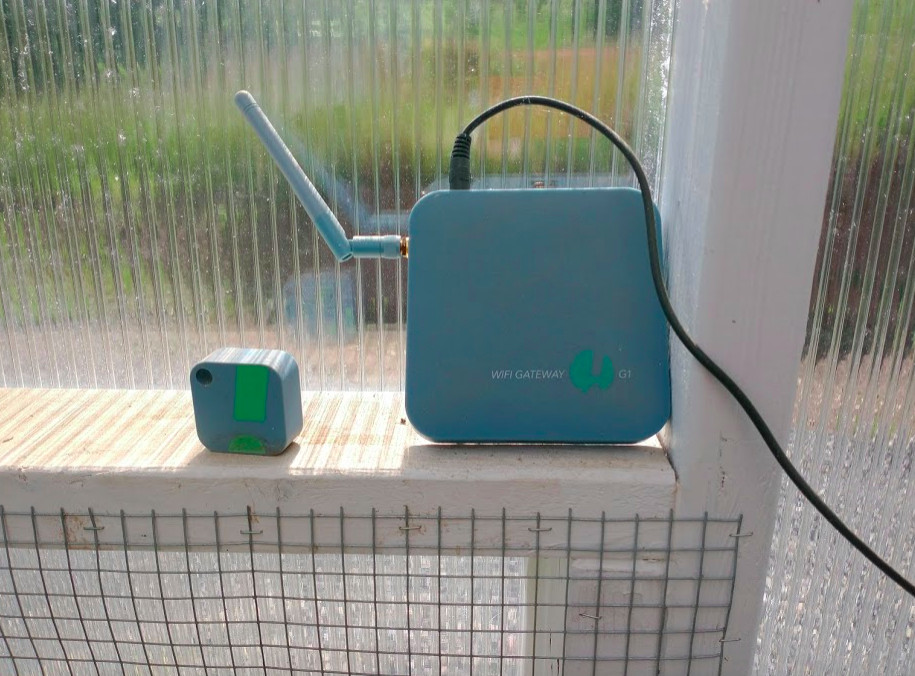 A remote temperature sensor shaped like a blue cube, next to a wi-fi gateway device which is also cubic but somewhat larger, and which has a short crooked antenna.