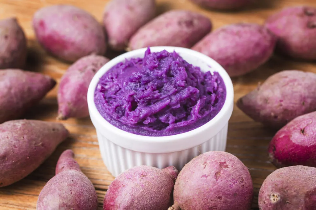 Red-purple skinned potatoes surround a small ramekin filled with purple mashed potatoes. 
