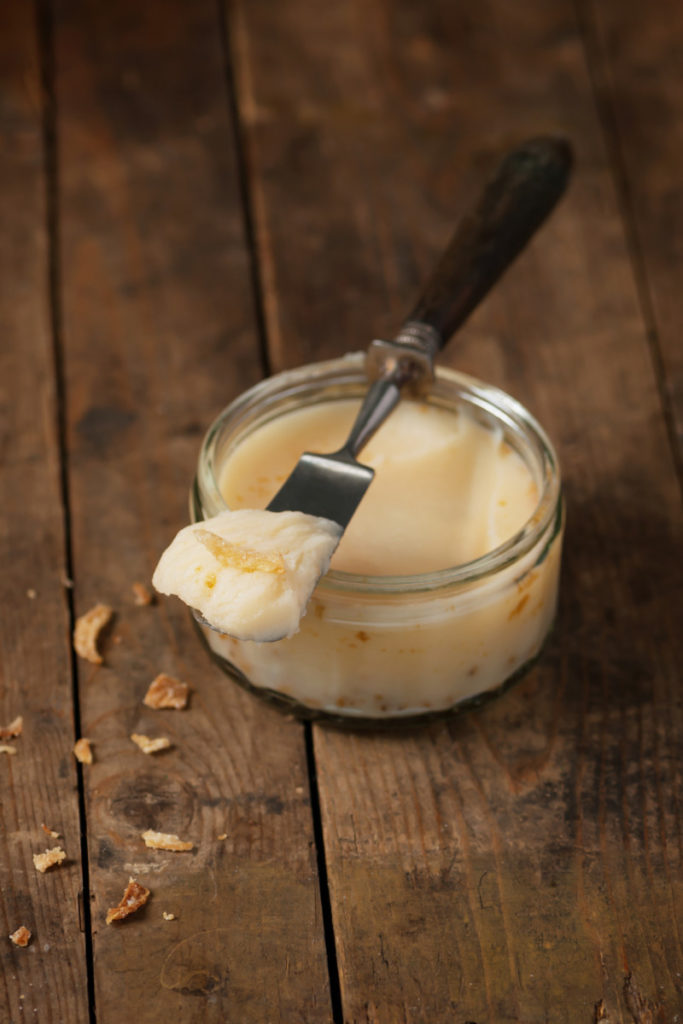 A small ramekin holds duck fat. A small wooden handled spreading knife has a scoop of duck fat on the blade.