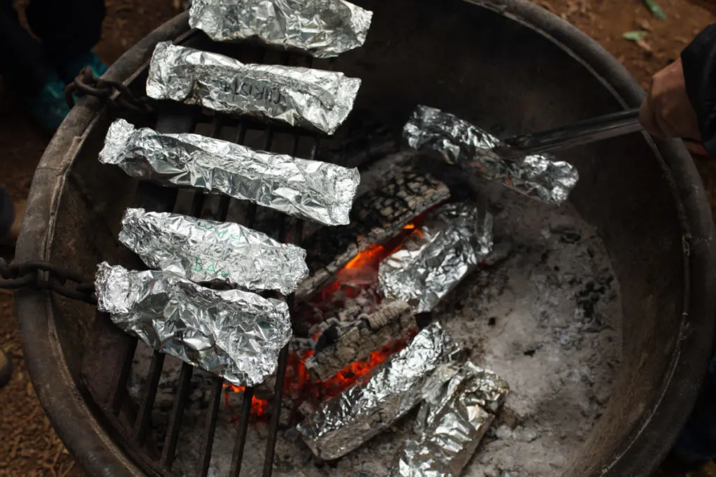 Several foil packet dinners are cooking in a fire in a fire pit.