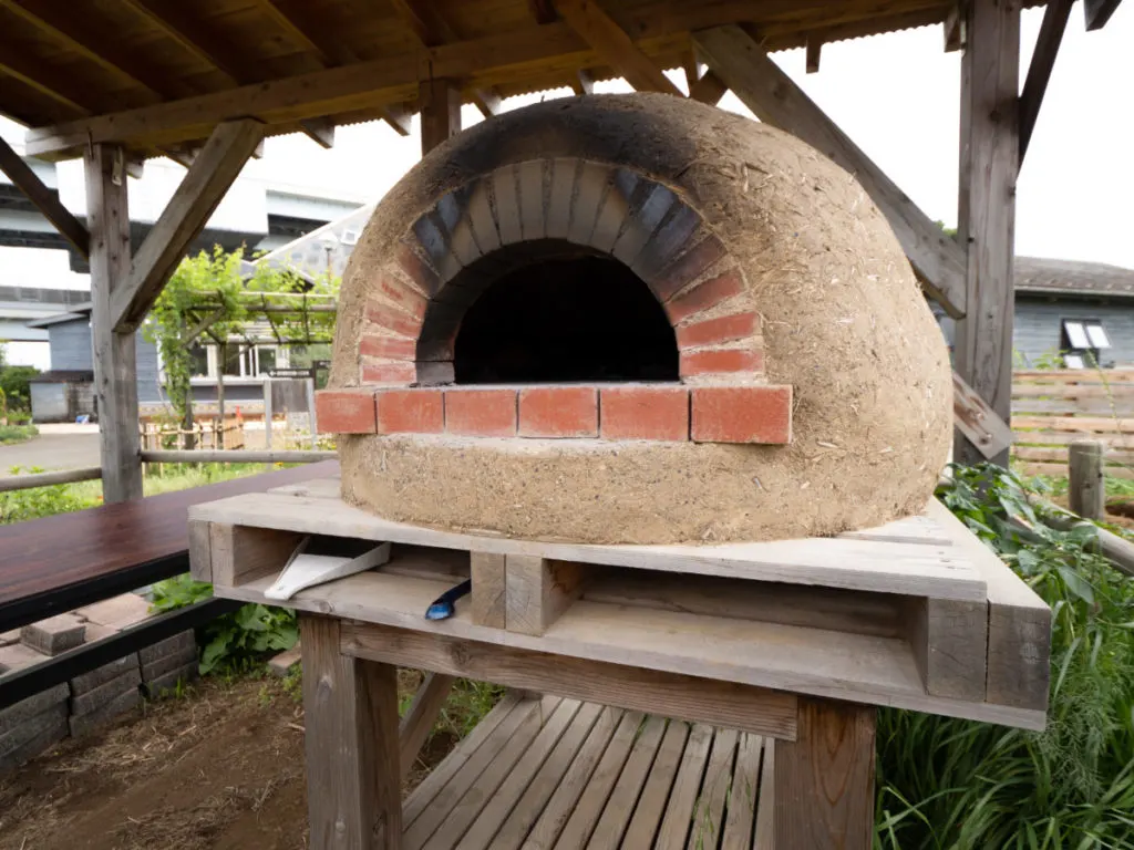 A large earth oven sitting on a wood support under a roof outside.