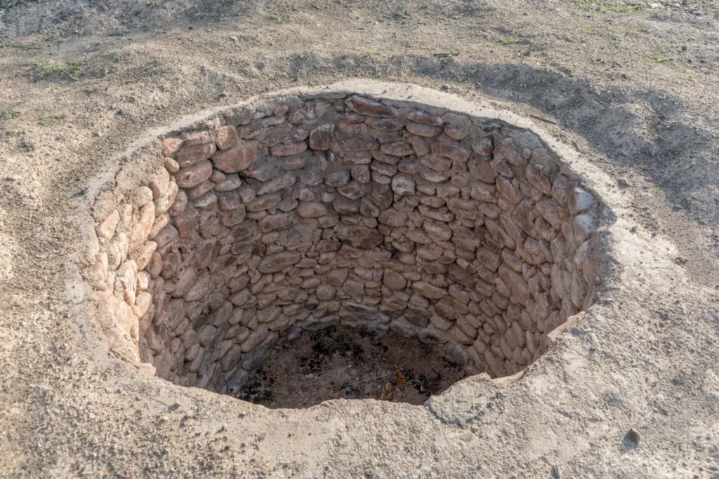 Overhead view of a traditional pit oven lined with small stones, dug into the earth.