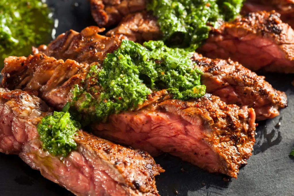 A grilled steak topped with bright green chimichurri.