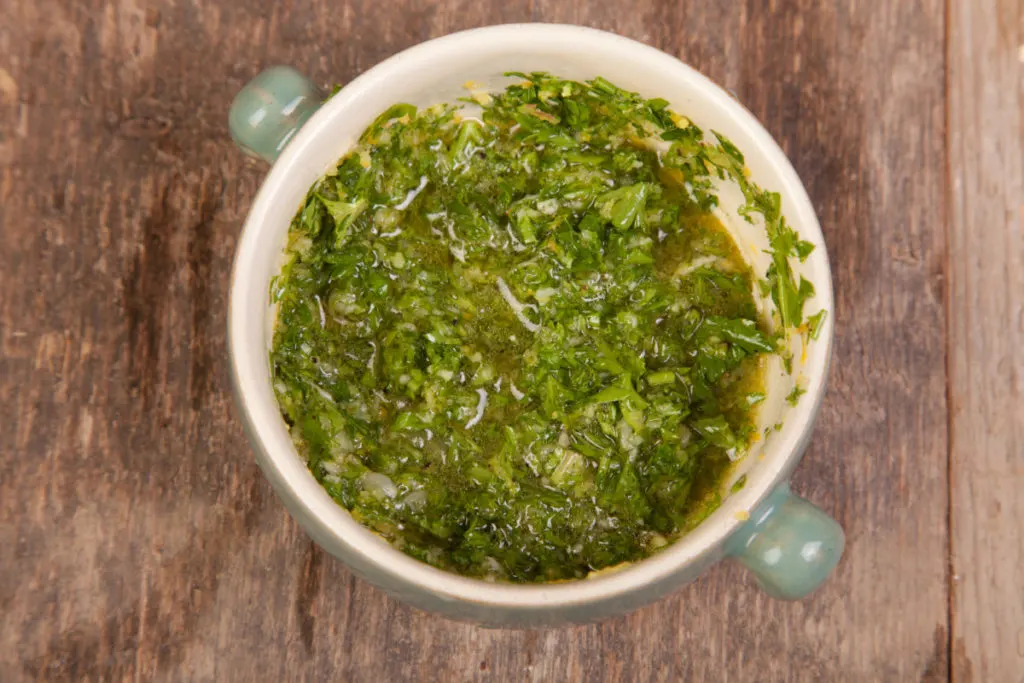 Overhead view of a bowl of gremolata sitting on a rough wood tabletop.