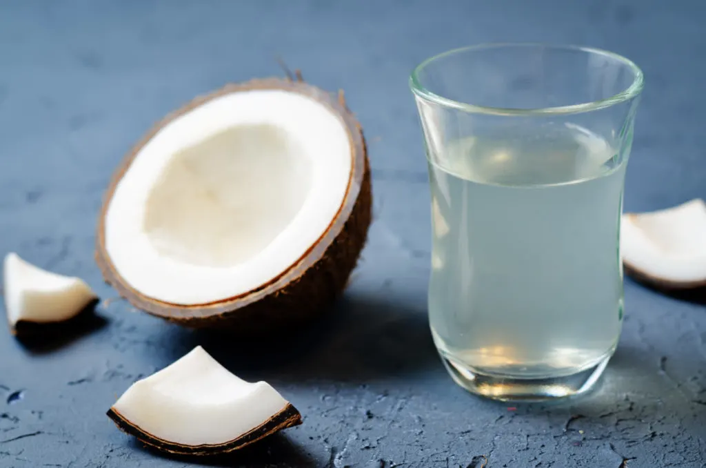 A glass of coconut water next to a broken coconut.