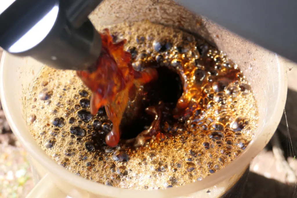 Overhead view of vermicompost tea coming from a spigot into a plastic pitcher. 