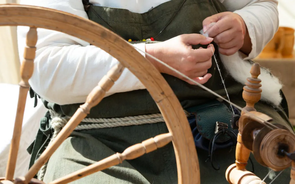 Close up of a woman sitting at a spinning wheel spinning angora rabbit wool.