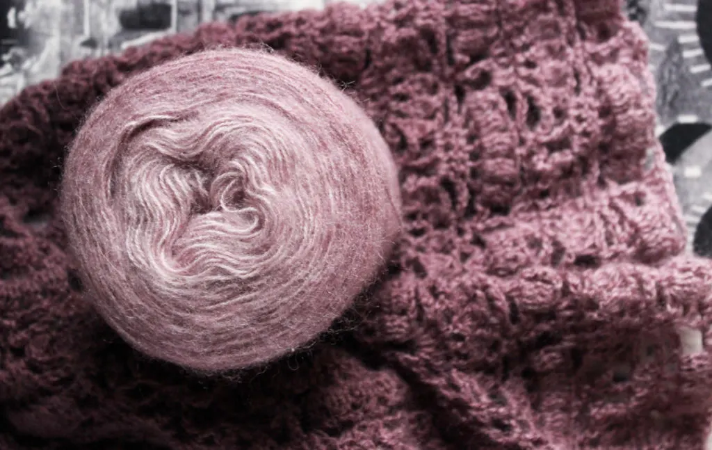 A beautiful lilac shawl knit from angora yarn. The ball of yarn sits on top of the finished shawl.