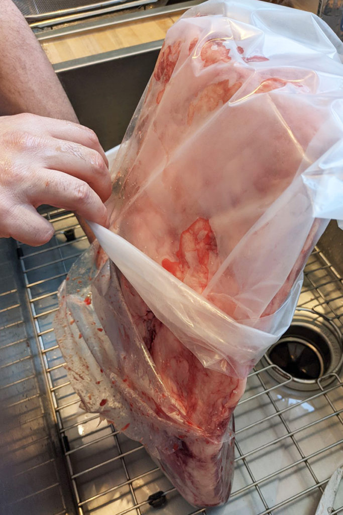 Matthew's hands shown sliding the store packaging off of the ribeye while rolling the vacuum bag over it.