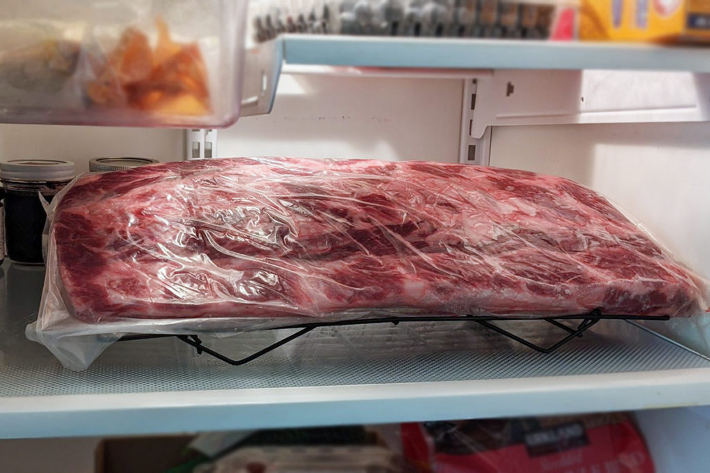 A whole ribeye sealed in a bag in a refrigerator.