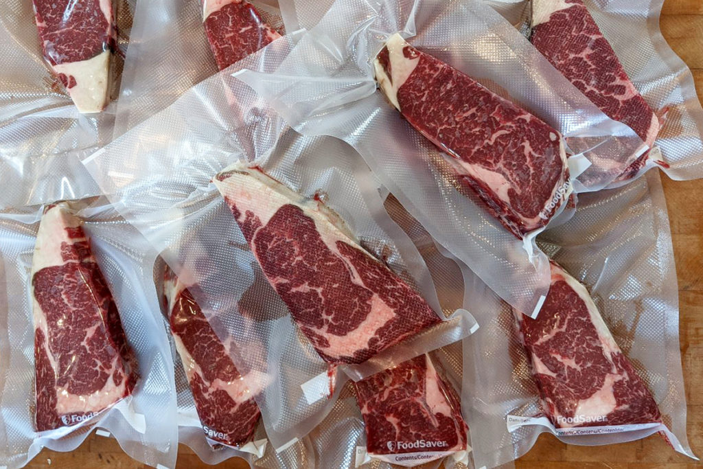 Overhead view of vacuum sealed dry-aged ribeye steaks on a butcher block. 