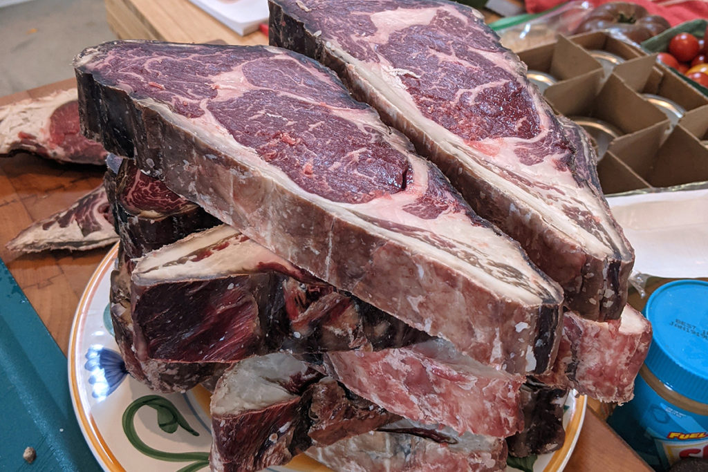 A large stack of steaks piled on a dinner plate waiting to be trimmed of the tough outer bark.
