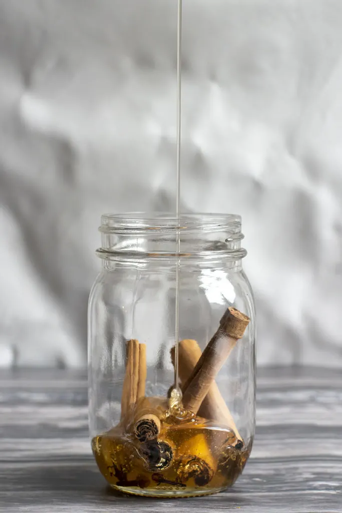 Jar filled with cinnamon sticks. We can see a thin drizzle of honey going into the jar. 