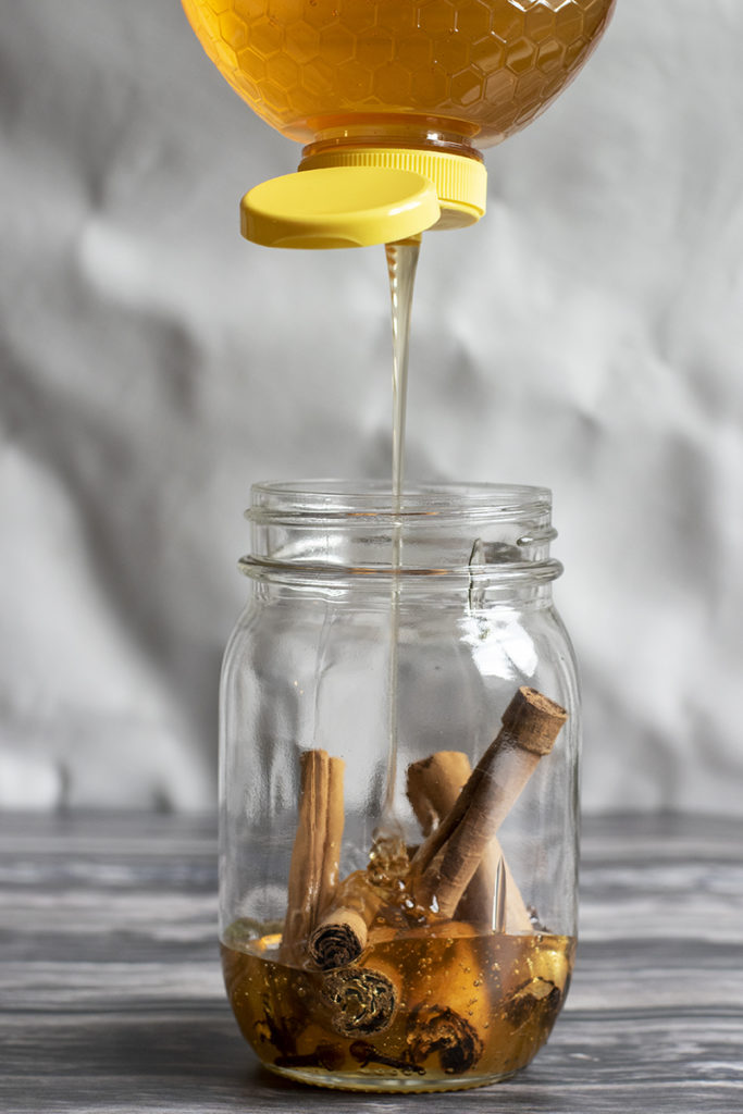 A bottle of honey upended drizzling honey into a jar of spices.