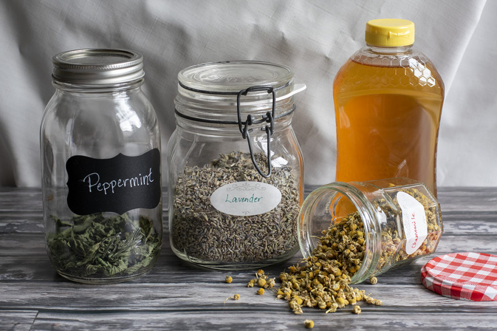 Jars of dried peppermint, lavender and chamomile with a bottle of honey. 