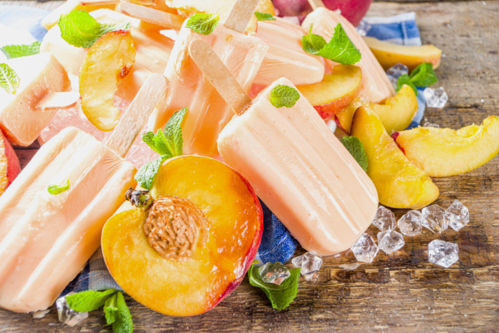 A pile of peach popsicles among peach slices and ice cubes