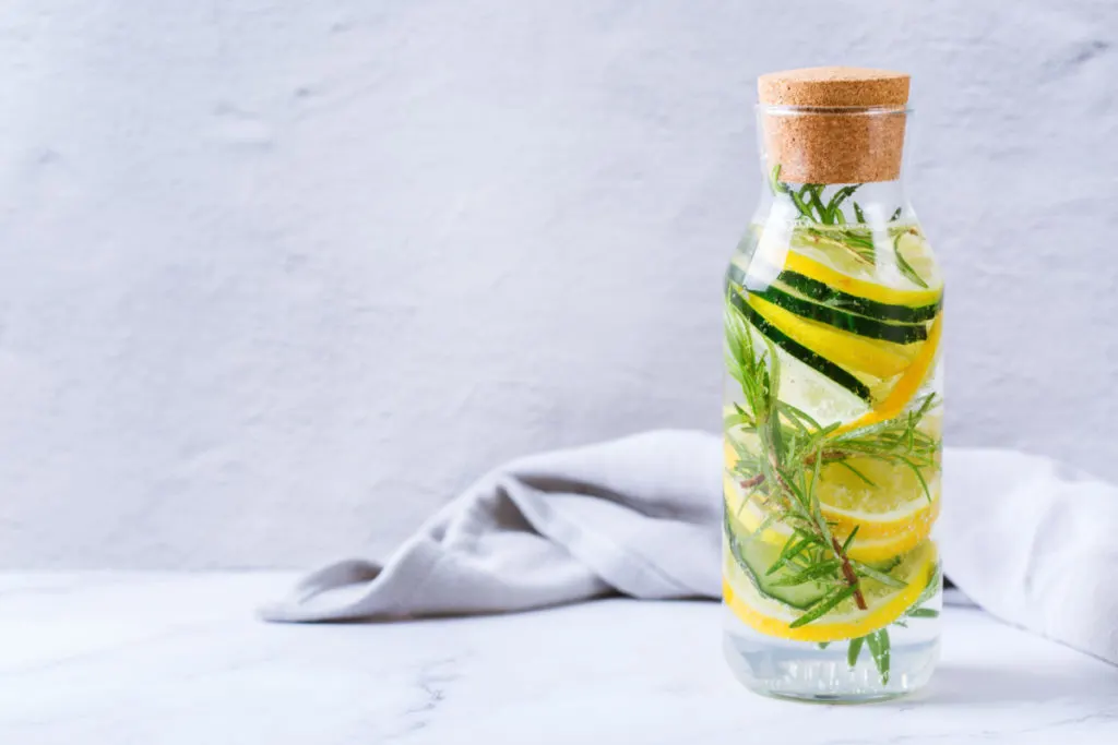 A bottle of cucumber slices, lemon slices and sprigs of rosemary filled with white vinegar