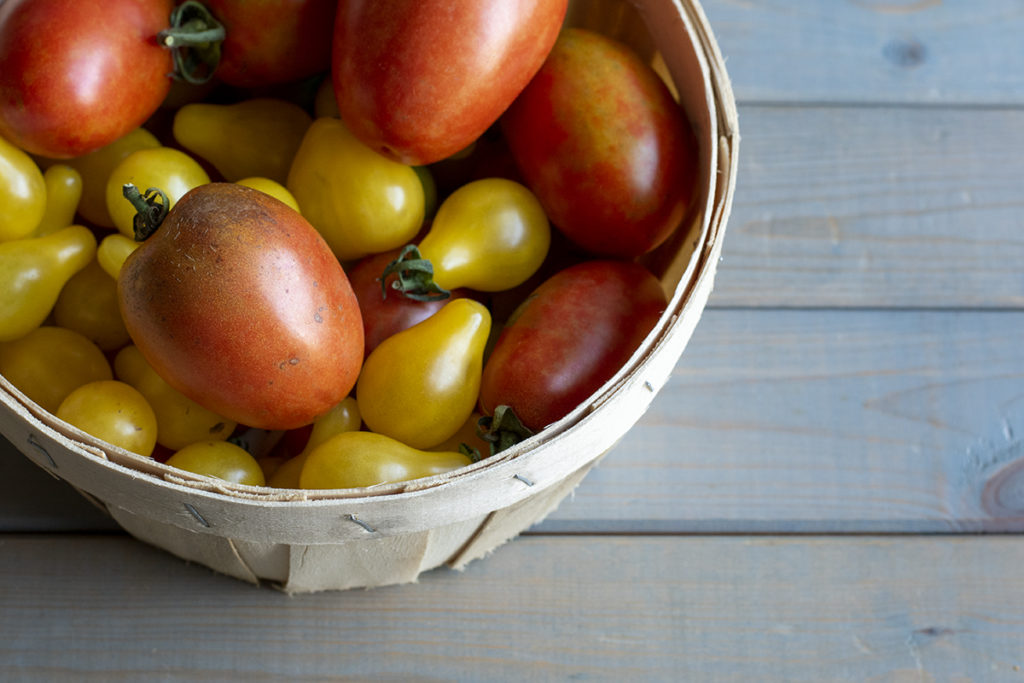 A small basket full of fresh yellow pear and Roma tomatoes.
