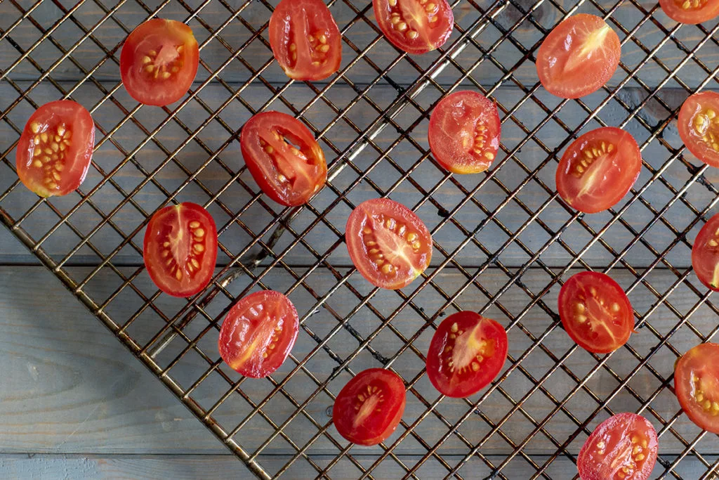 A wire cooling rack with the cherry tomato halves spaced apart on it.