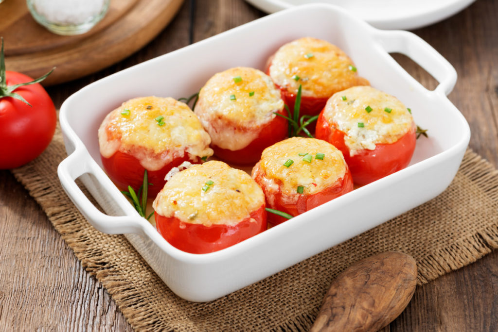 White casserole dish with six cheesy stuffed tomatoes in it