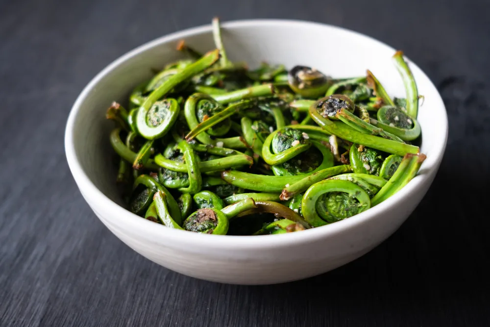 A white bowl of sautéed fiddleheads with minced garlic. 